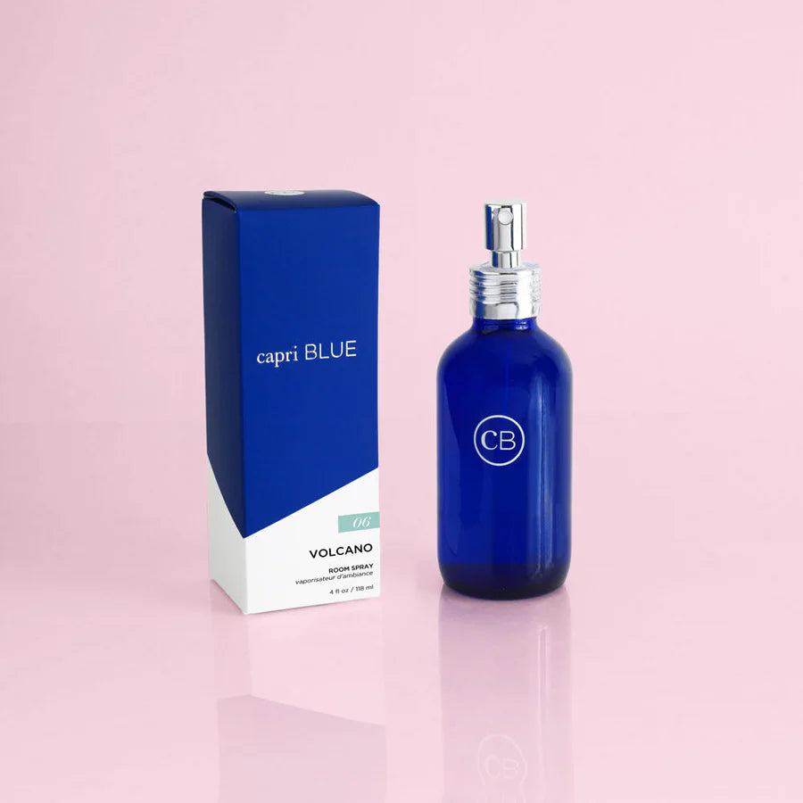 A blue room spray bottle with a white label that reads 'CP' and the word 'VOLCANO' on the lid, next to its blue and white box packaging, against a pink background.