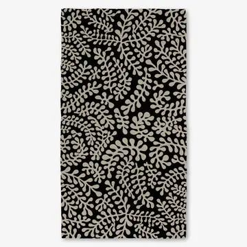 This image features the TANGLED LUXE BATH TOWEL, displayed vertically. The towel showcases an elegant and intricate leaf pattern in a subtle beige color on a black background.