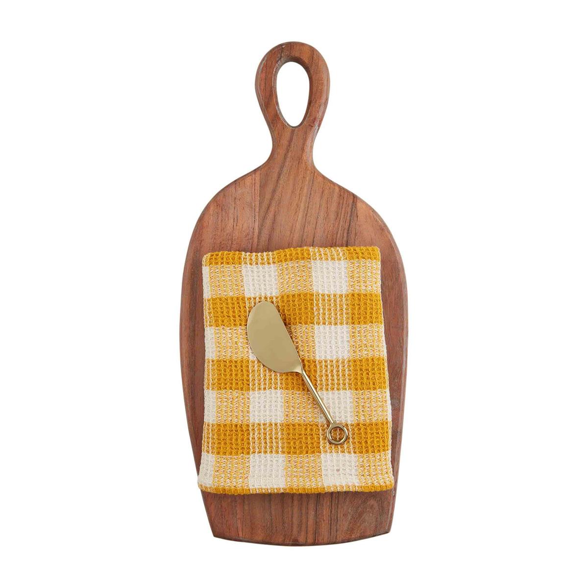 A wooden cheese board set with a yellow and white checkered towel on top and a metal cheese knife.