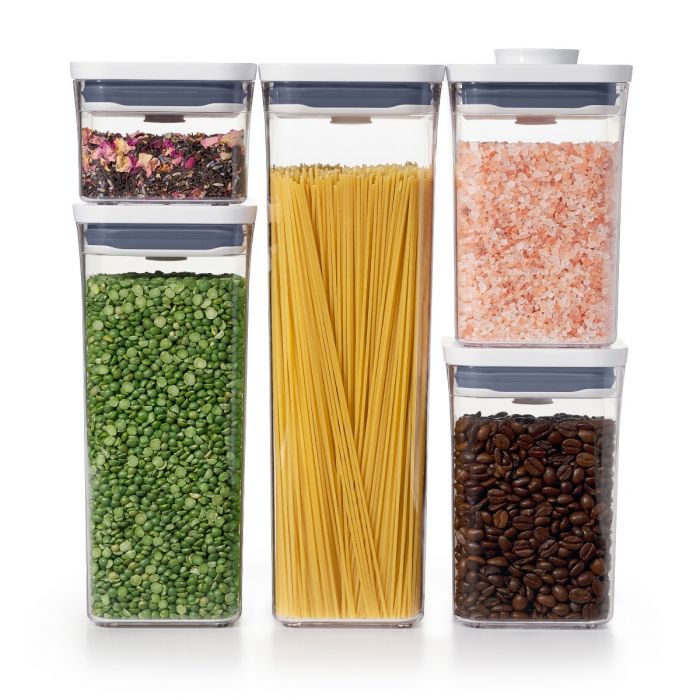 A set of five OXO Good Grips food storage containers in various sizes, filled with different colored contents such as flour, coffee, and spices.