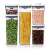 A set of five OXO Good Grips food storage containers in various sizes, filled with different colored contents such as flour, coffee, and spices.
