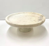 A white marble cake stand with a round flat top and a cylindrical pedestal base.