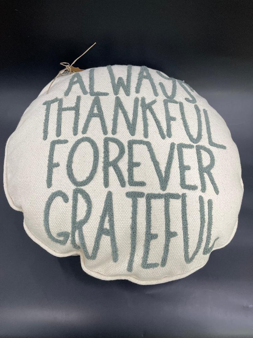 A round white holiday pillow with the text 'ALWAYS THANKFUL FOREVER GRATEFUL' embroidered in gray.
