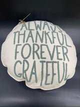A round white holiday pillow with the text 'ALWAYS THANKFUL FOREVER GRATEFUL' embroidered in gray.