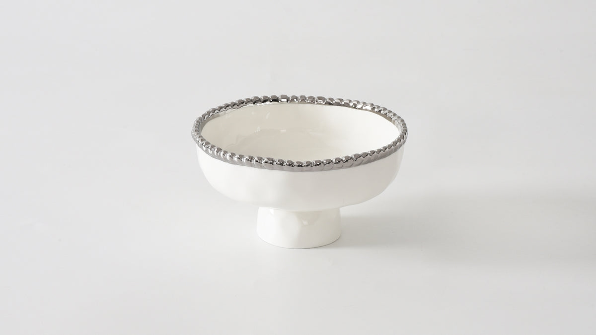 A small, silver-footed white bowl with a decorative edge on a plain background.