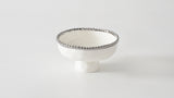 A small, silver-footed white bowl with a decorative edge on a plain background.