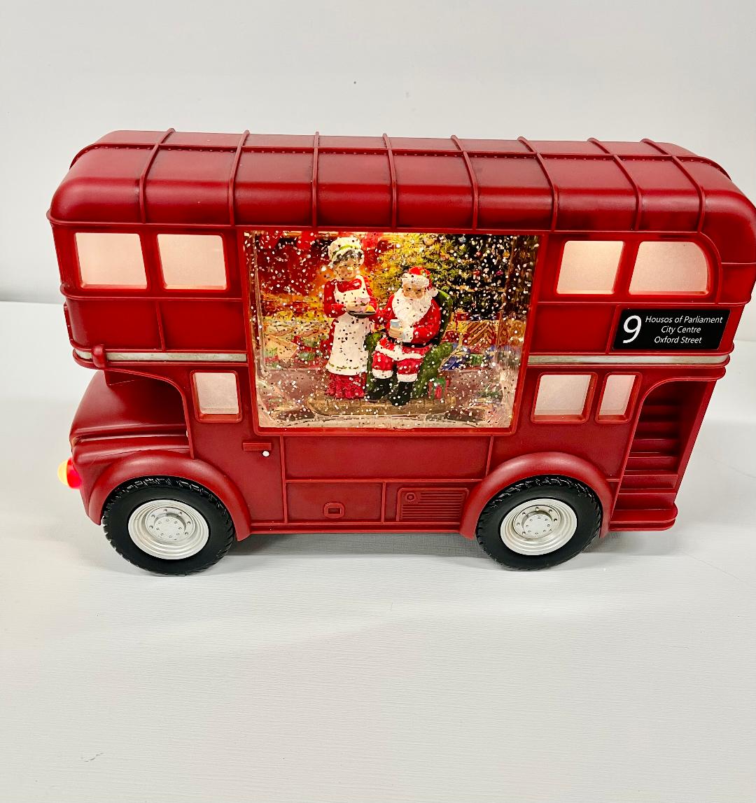 A decorative holiday-themed train set with a red bus and a Christmas scene displayed on the side.