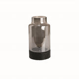 A cylindrical glass vase with a metallic top and a black clay base.