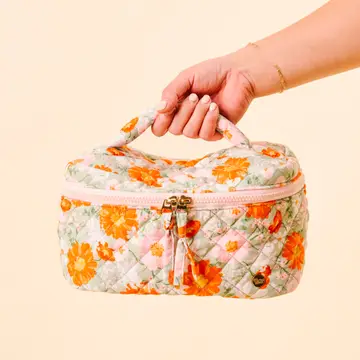 A hand holding a floral cosmetic bag with a zippered top and a handle.