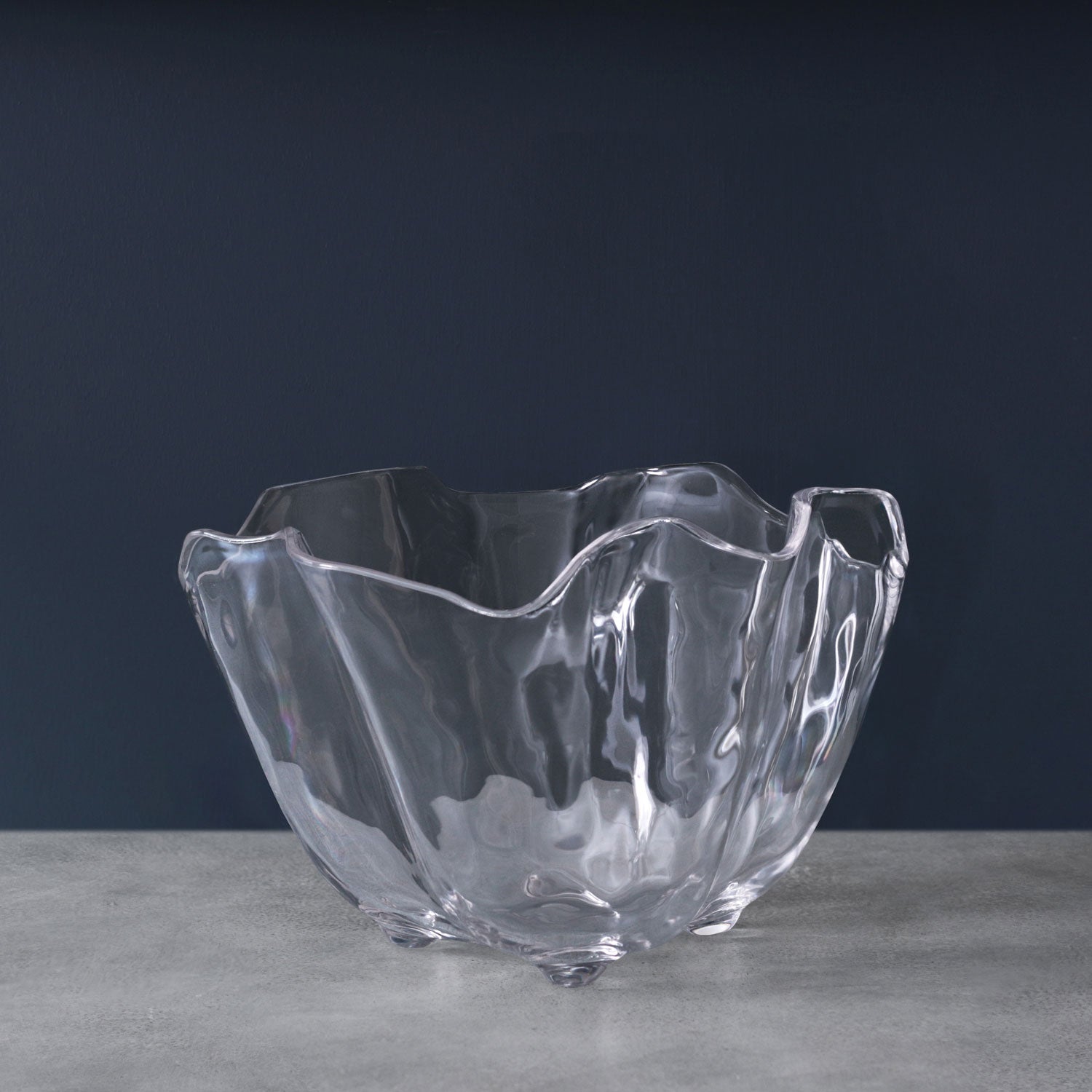A clear acrylic ice bucket with a geometric cut design, placed on a grey surface with a navy background.