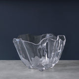 A clear acrylic ice bucket with a geometric cut design, placed on a grey surface with a navy background.