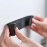 A set of black plastic pan lid holders being attached to a white surface.