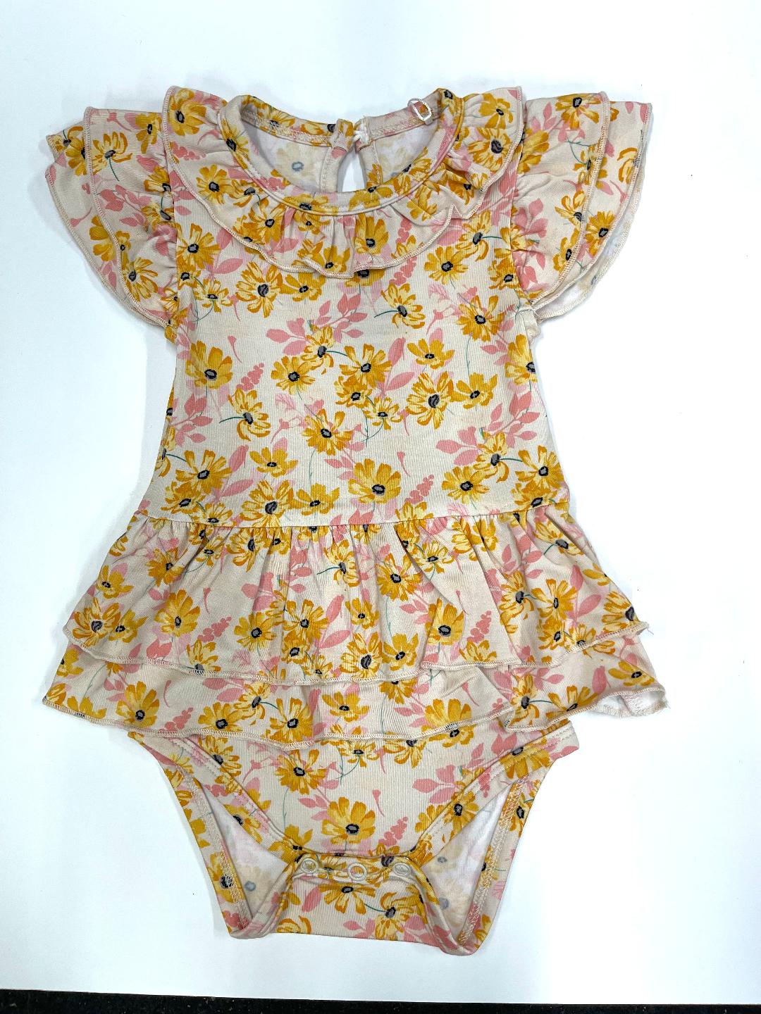 A baby onesie with a floral pattern featuring daisies in yellow and pink colors on a beige background.