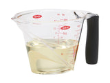 A clear plastic measuring cup with angled markings for measuring ingredients, featuring an angled design to view measurements easily, with a black handle.