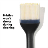 A silicone pastry brush with a black handle and white bristles, with a label that reads 'Brushes won't clump during cleaning'.