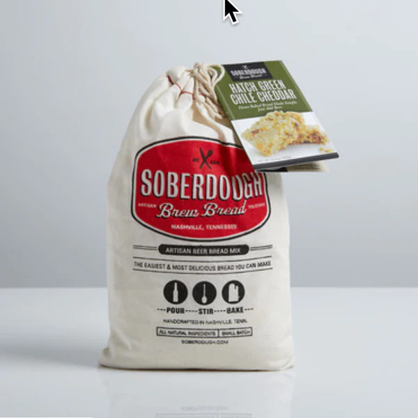 A paper bag labeled 'Soberdough Bread Mix' with a window showing the product inside. The bag has a red and white color scheme and text detailing the product's features.